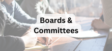 Group of people sitting at a table writing and discussing together, with the text "Boards & Committees" displayed. 