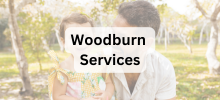 Adult and child sitting together outdoors in a park setting, with the text "Woodburn Services" displayed.