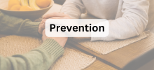 Two people sitting at a table holding hands in a supportive gesture, with the text "Prevention" displayed.